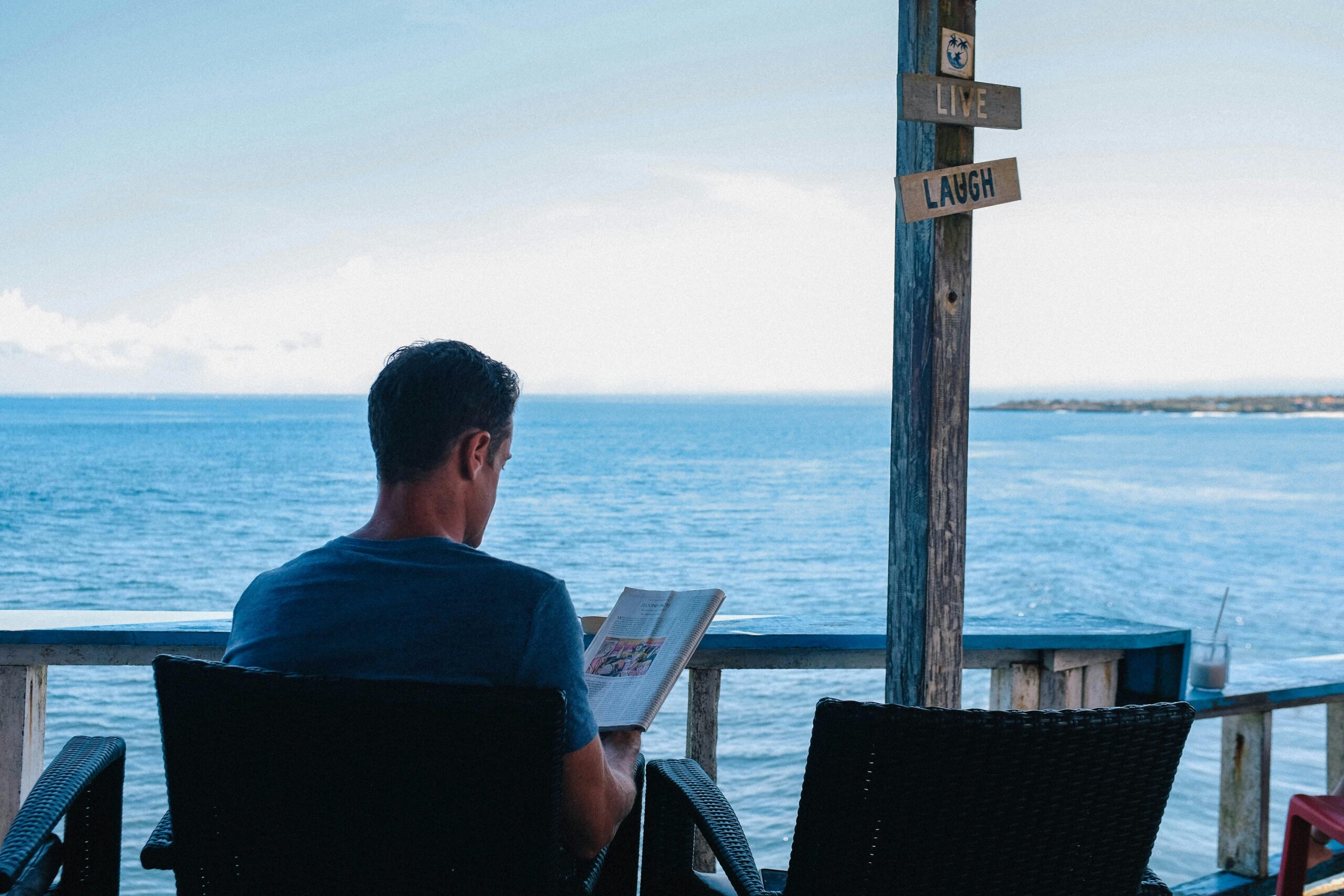 A man relaxes with a book overlooking the ocean in Bali, enjoying leisure time.