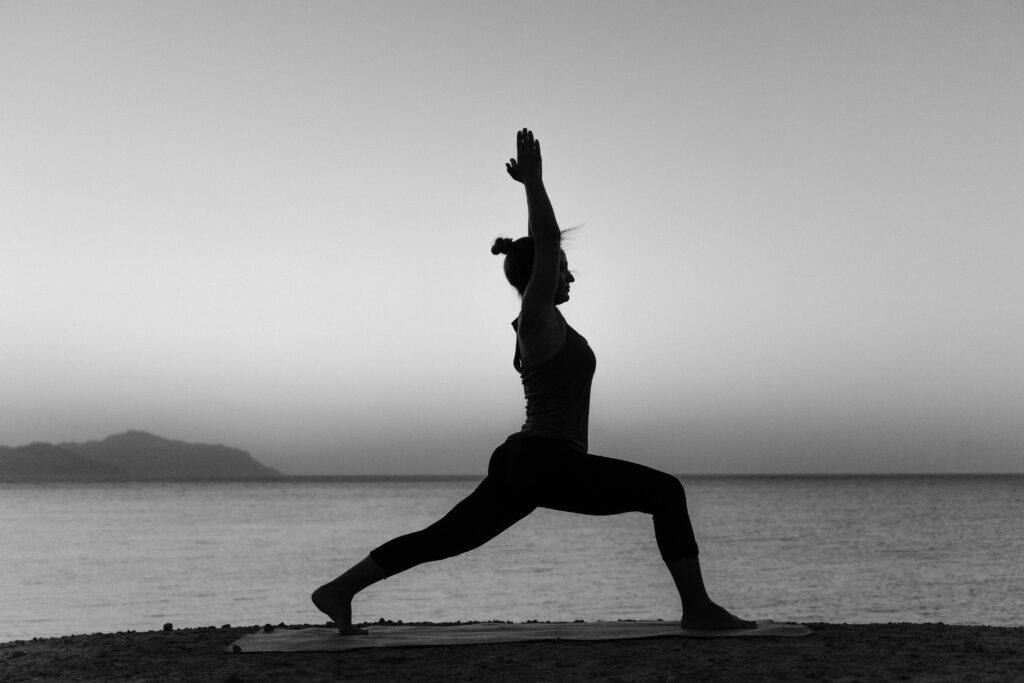 Grayscale silhouette of a woman practicing yoga on a beach at sunset.