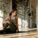 A woman does a yoga pose on a mat in a bright, minimalist studio.