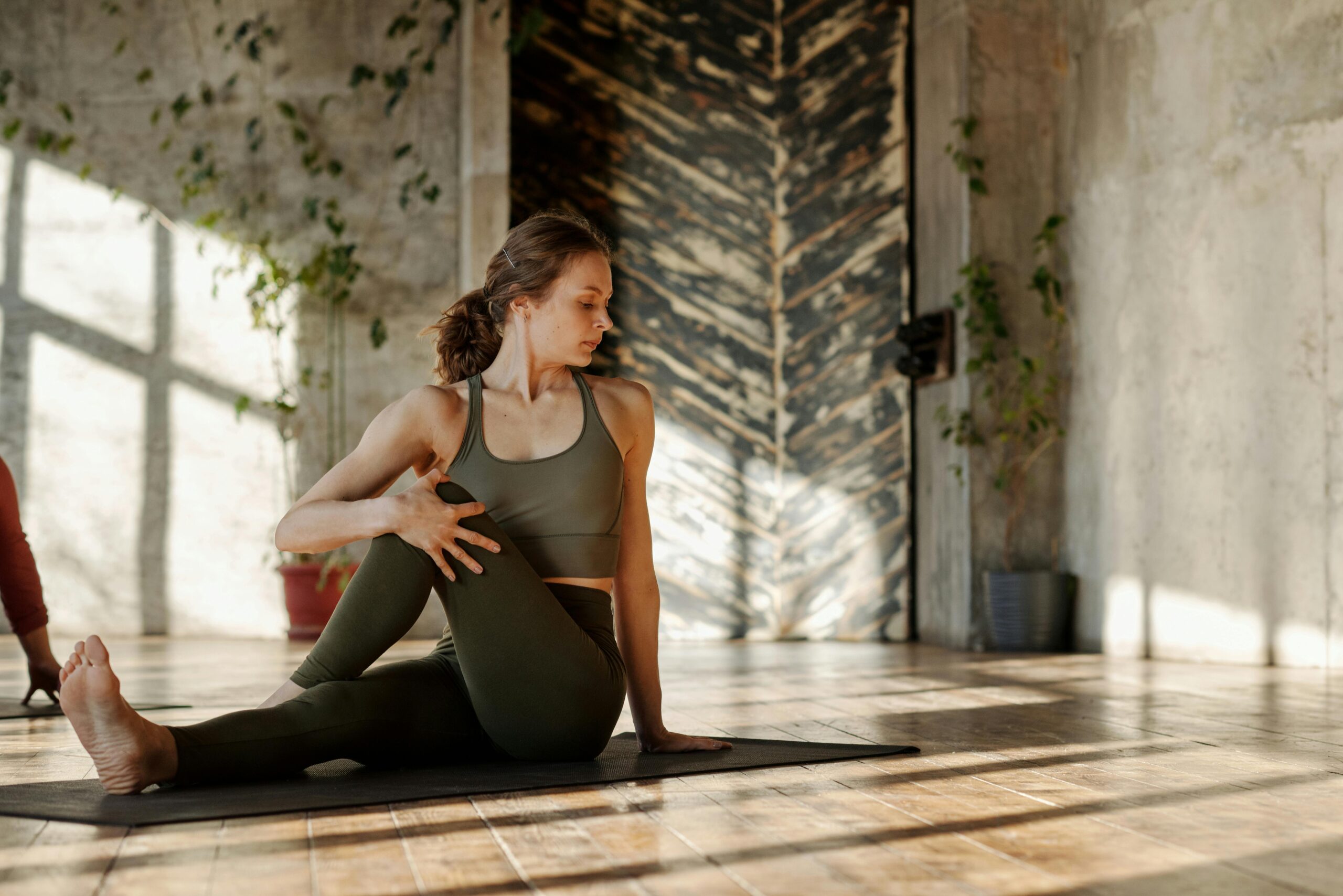 A woman does a yoga pose on a mat in a bright, minimalist studio.
