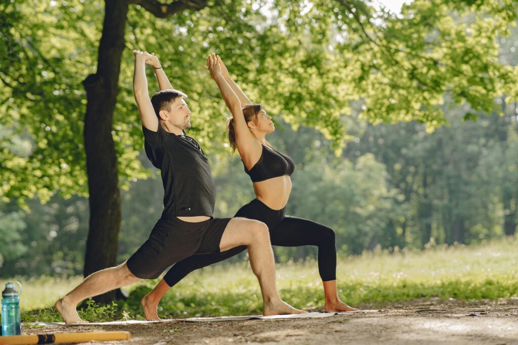 Couple practicing yoga outdoors in a serene park surrounded by nature.