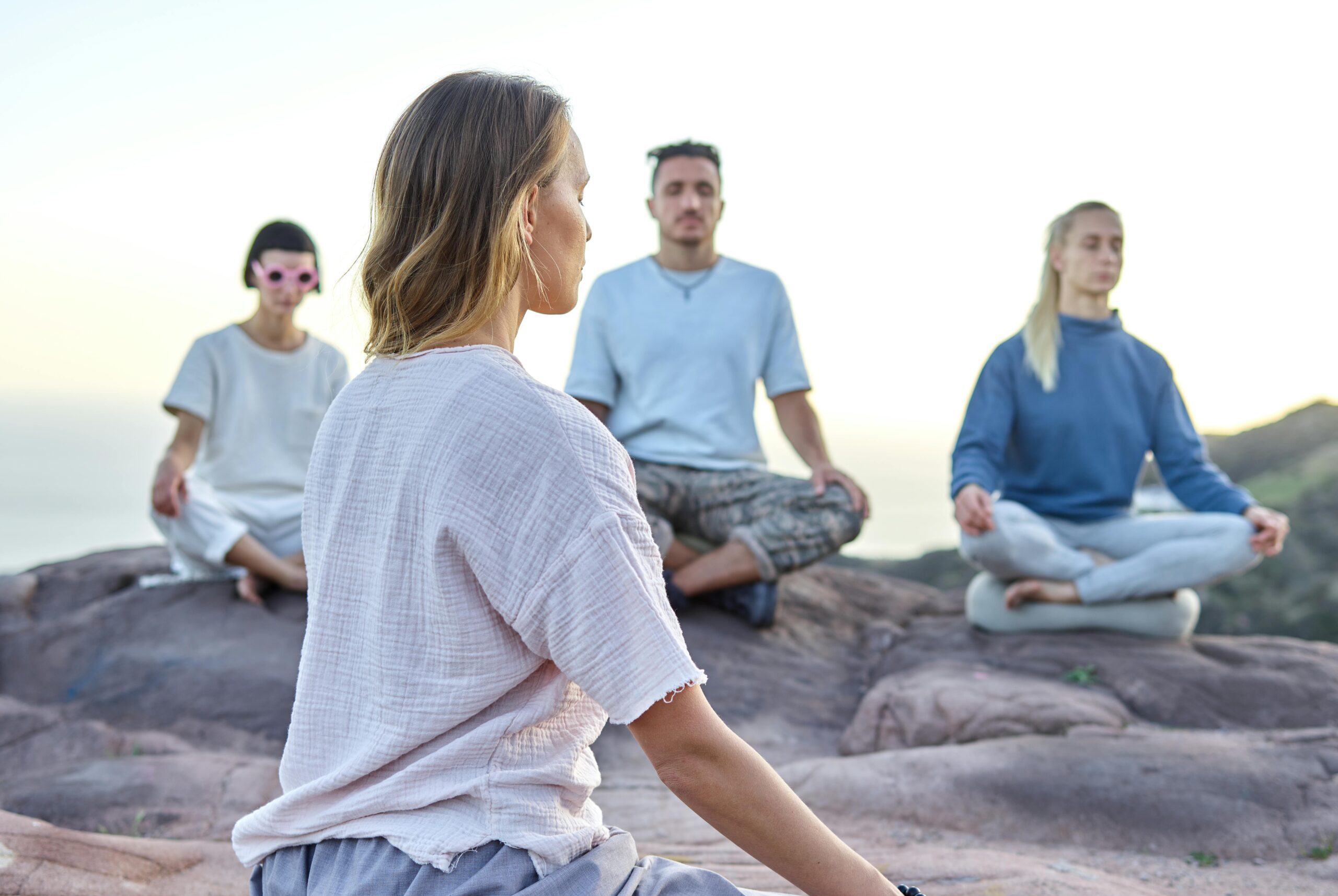 Group of adults meditating on a rocky cliff at sunset, embracing relaxation and spirituality.
