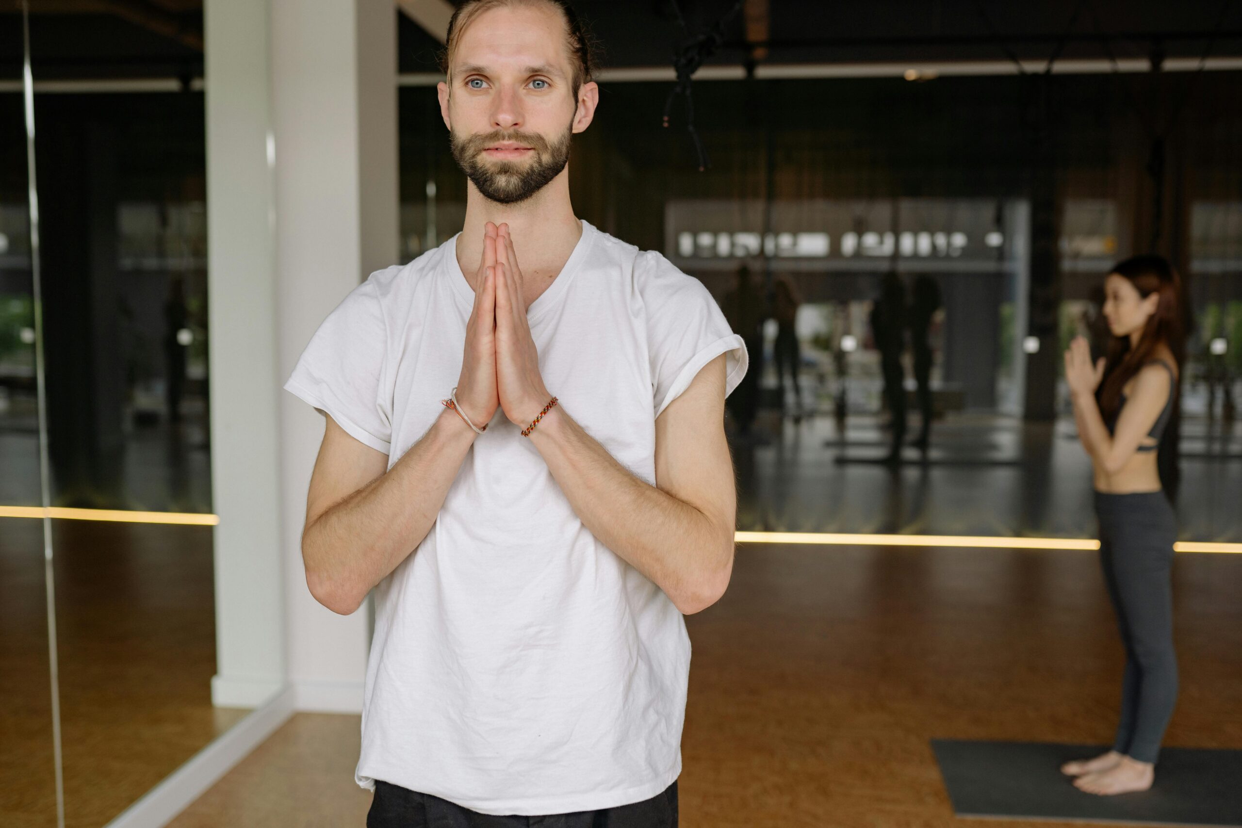 A man in a white shirt practicing yoga in a calm indoor studio, exemplifying mindfulness and relaxation.