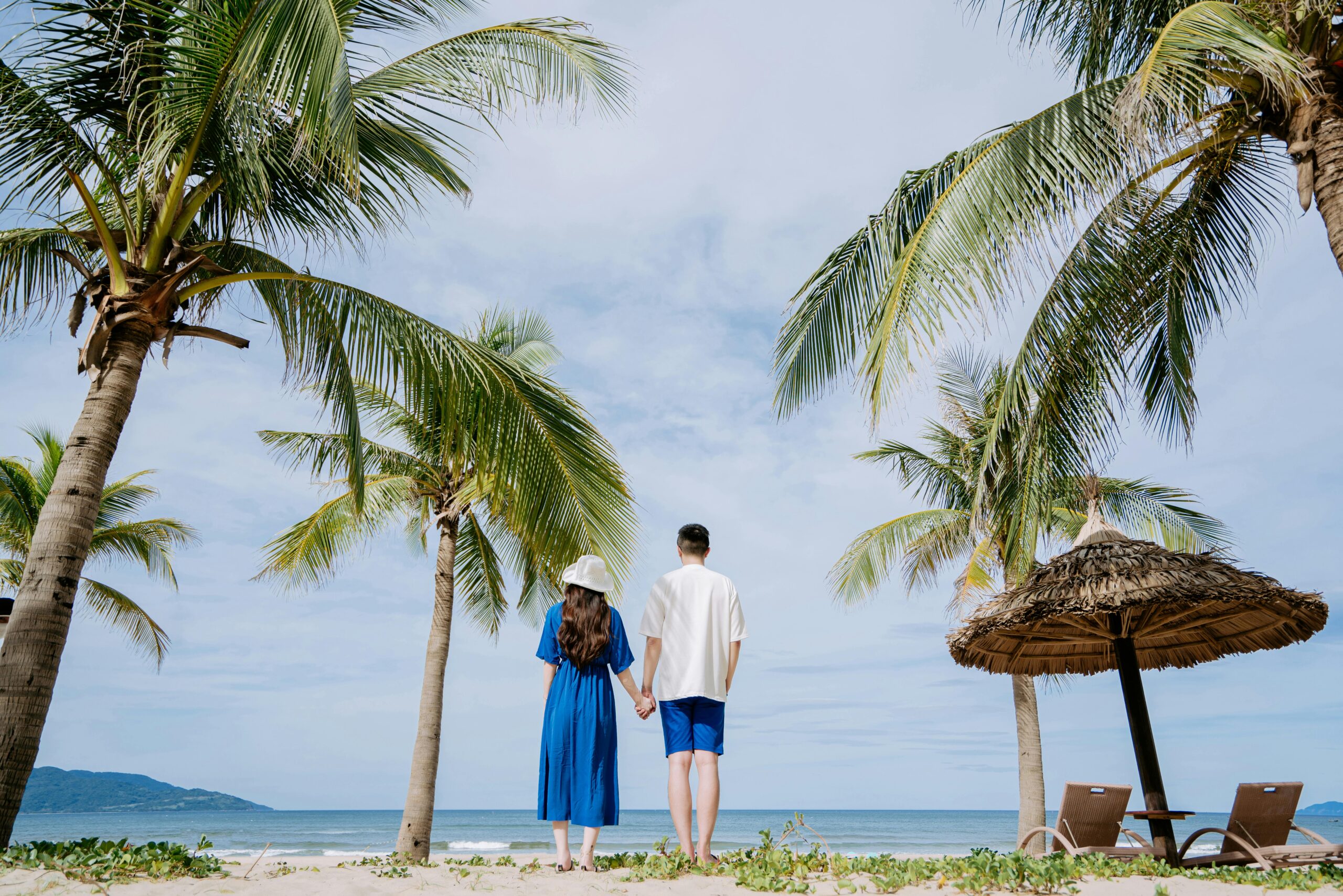 Couple holding hands on a tropical beach surrounded by palm trees, enjoying a serene vacation.