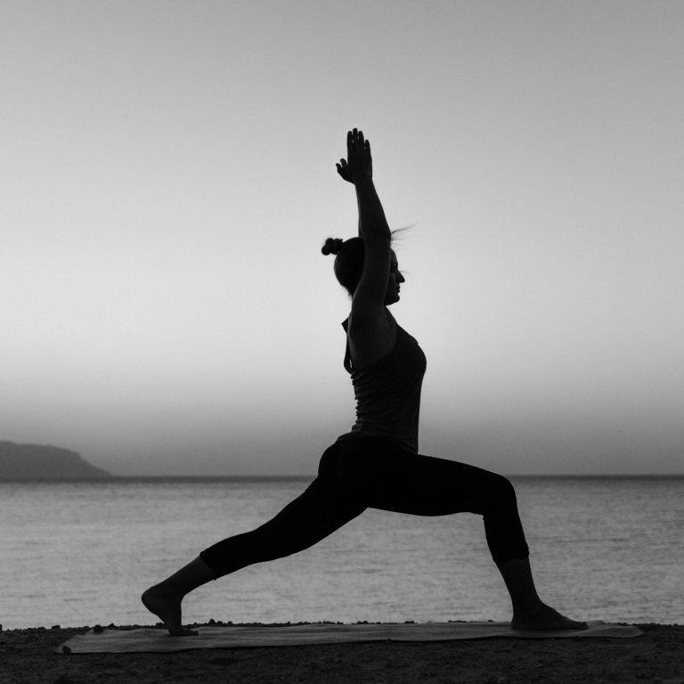Grayscale silhouette of a woman practicing yoga on a beach at sunset.